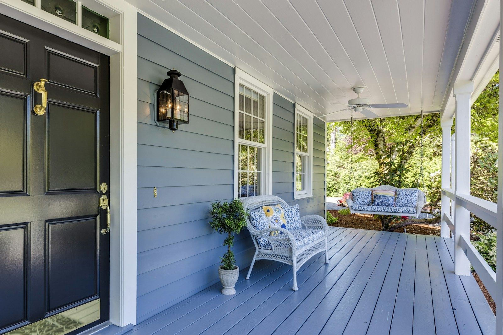 Blue front porch with a black door and white wicker chairs