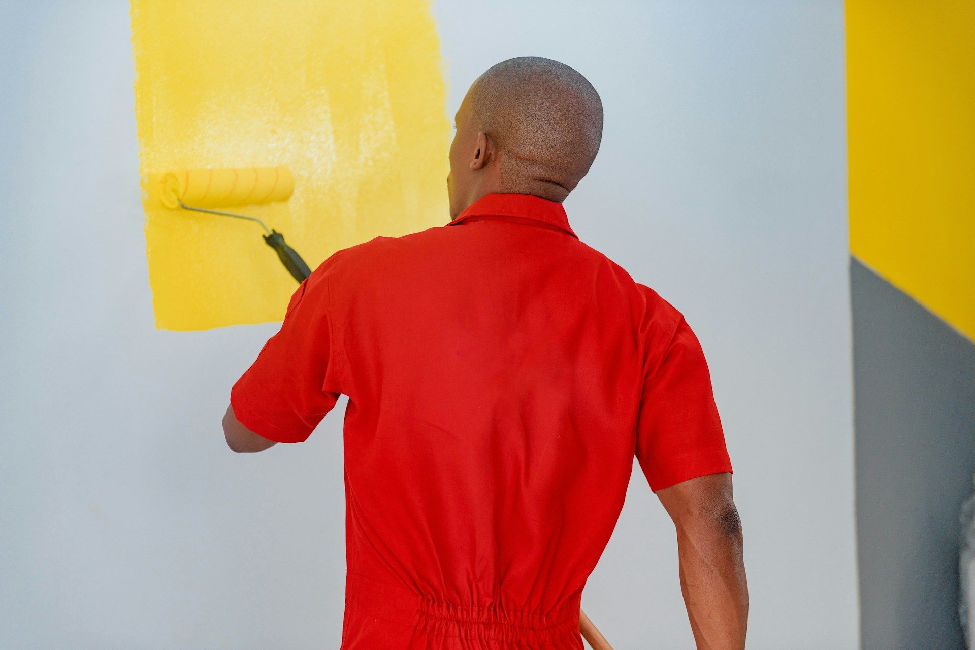 A decorator painting a wall a bold yellow with a roller