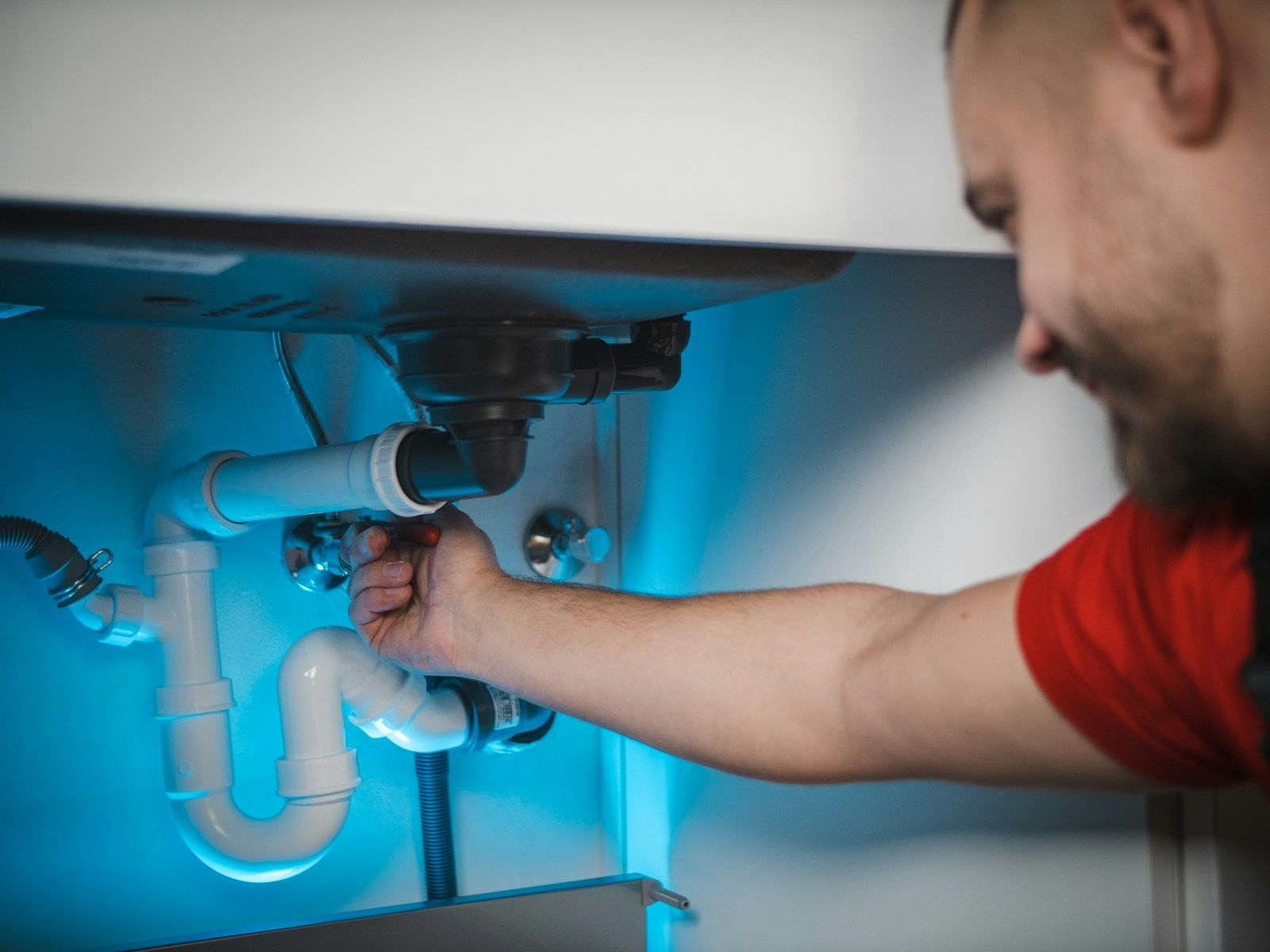 A plumber working on a pipe inside a wall